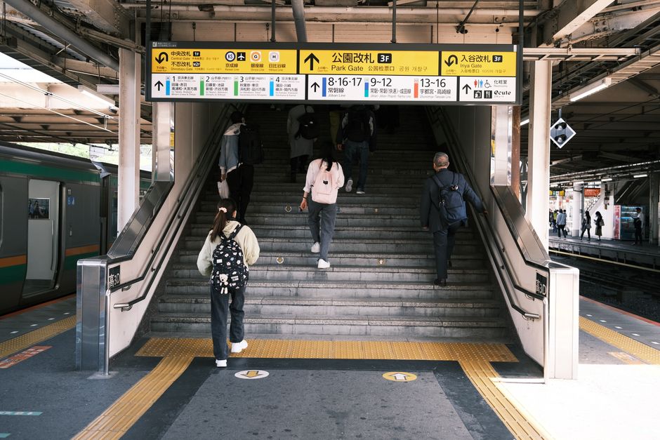 A person with a backpack descending an escalator at Sutton station, which features a modern interior with metal support beams, tiled floors, and glass panels. The escalator is clean and well-lit, with